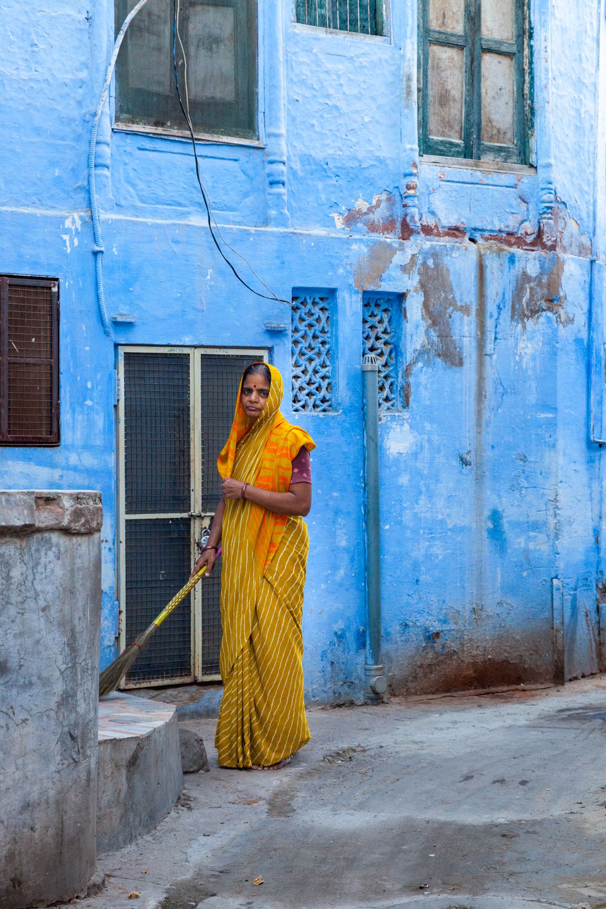 Woman in a yellow sari sweeping in front of a blue wall