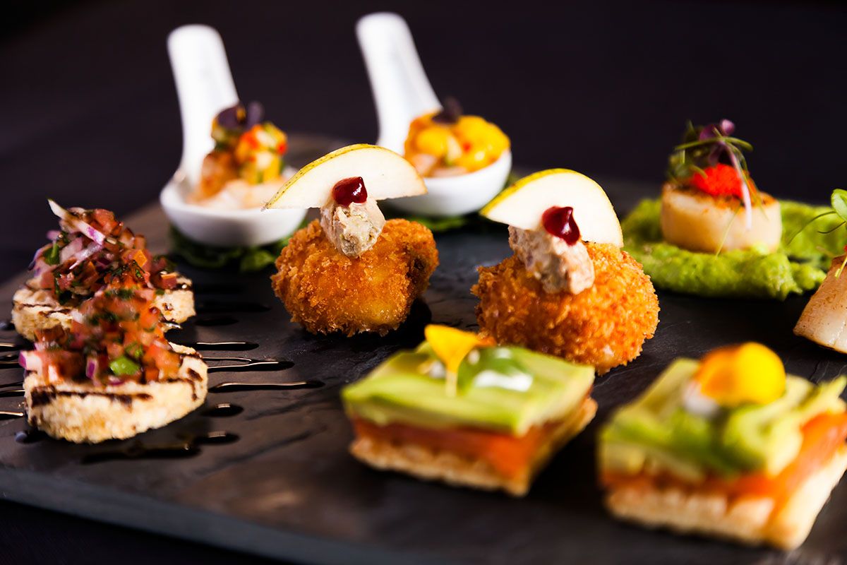 Canapés on black slate, including spoons of salsa and crumbed bites topped with pear