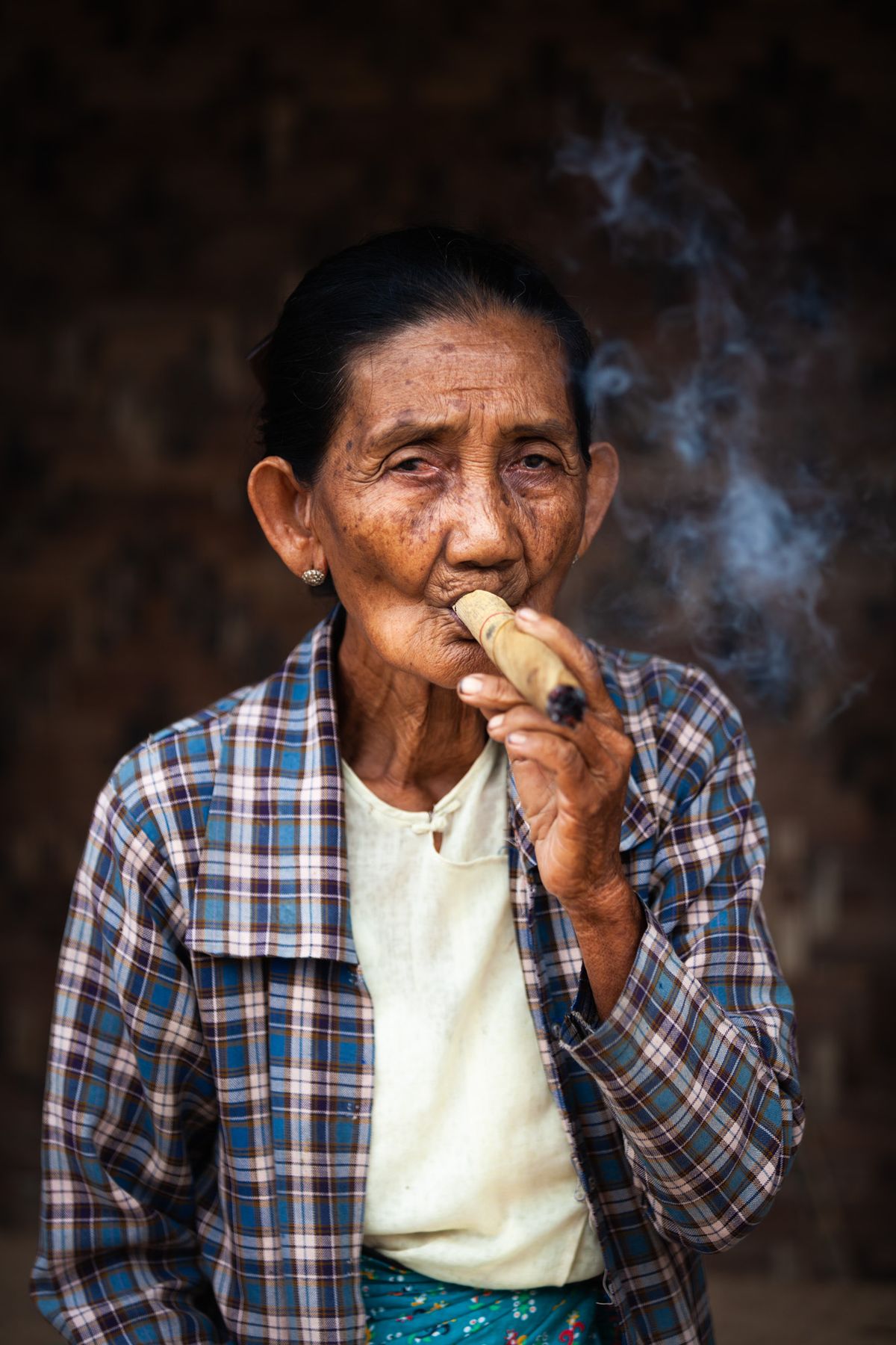 Elderly woman in a plaid shirt smoking a cheroot