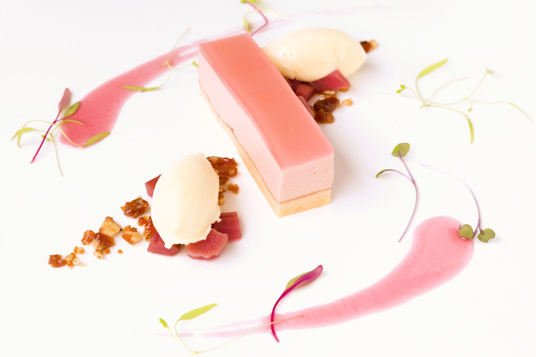 Pink rhubarb dessert bar with two quenelles of ice cream on white