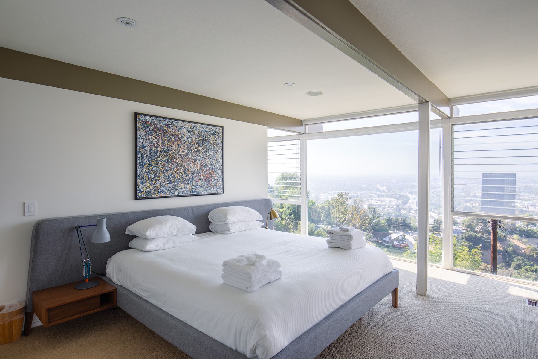 White bedroom with floor-to-ceiling windows looking over a hazy city