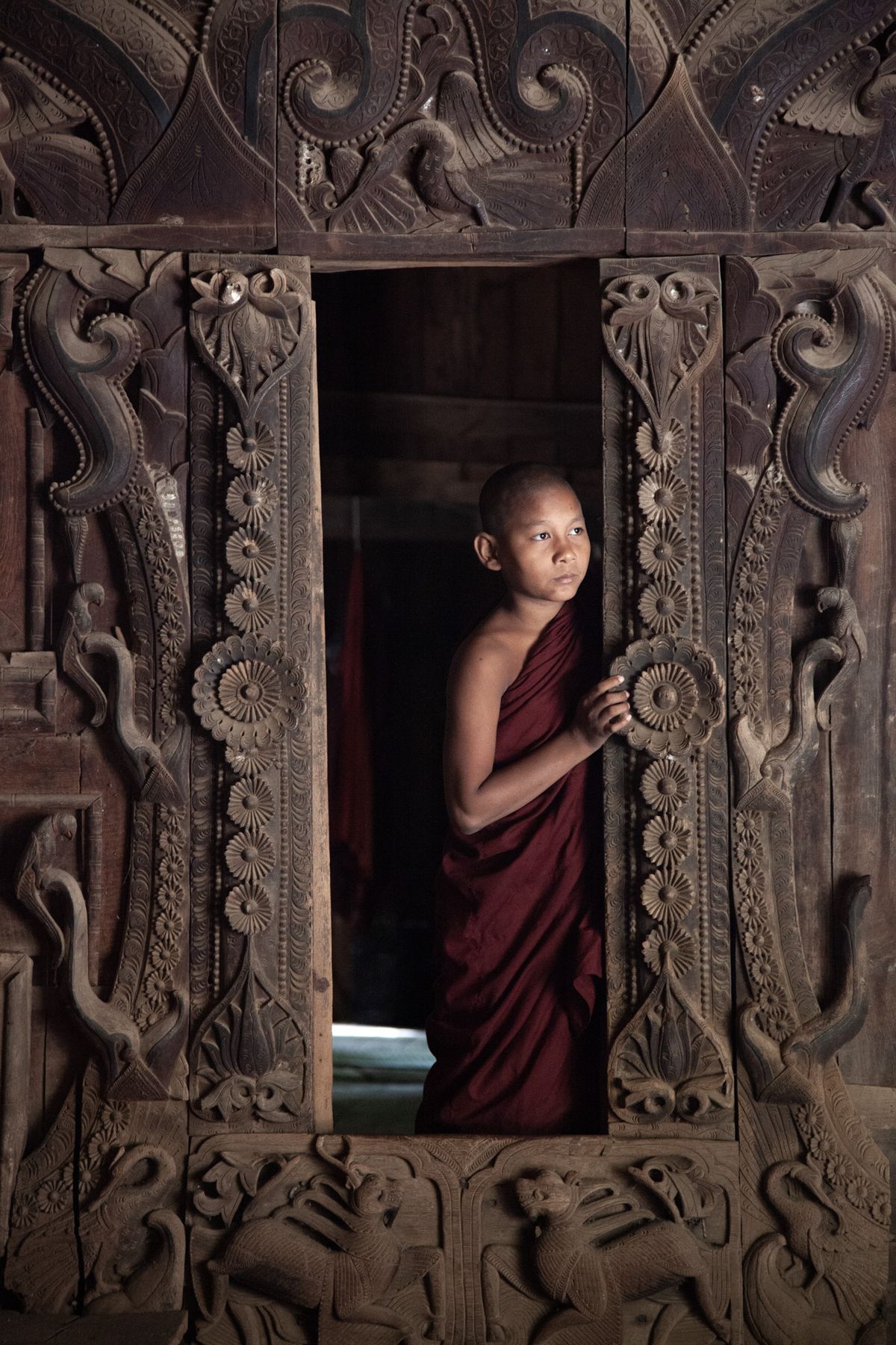 Young monk looking out from a carved teak window