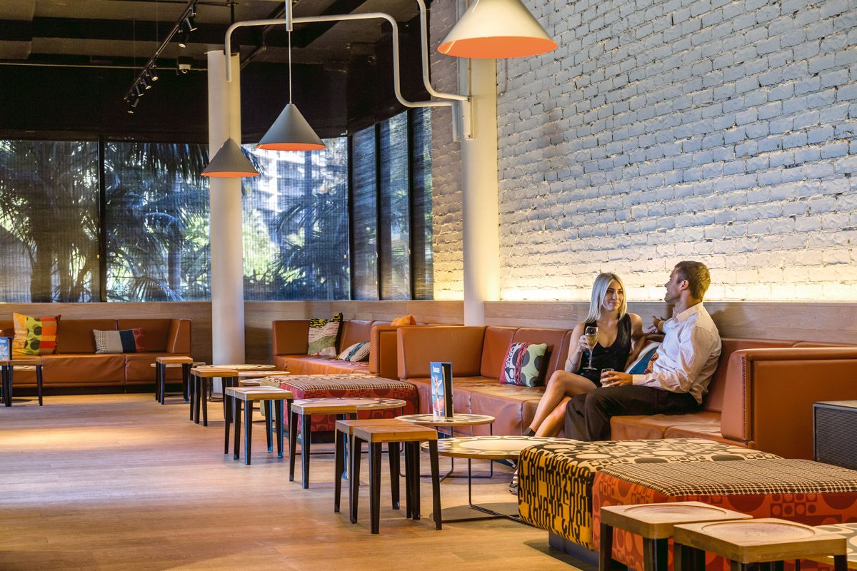 Couple talking on a leather banquette in a lounge with a white brick wall