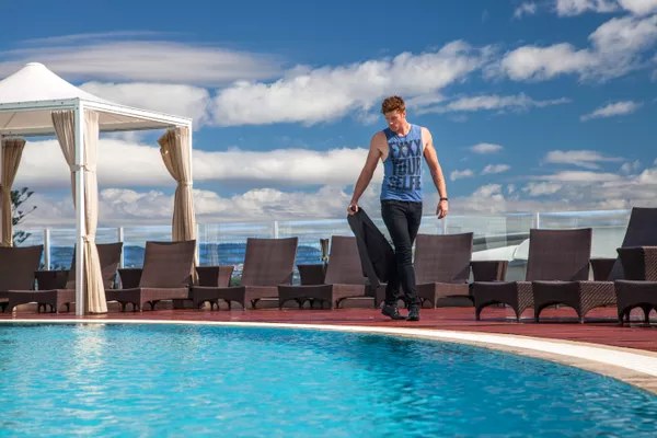 Man walking past a rooftop pool with cabanas and ocean behind